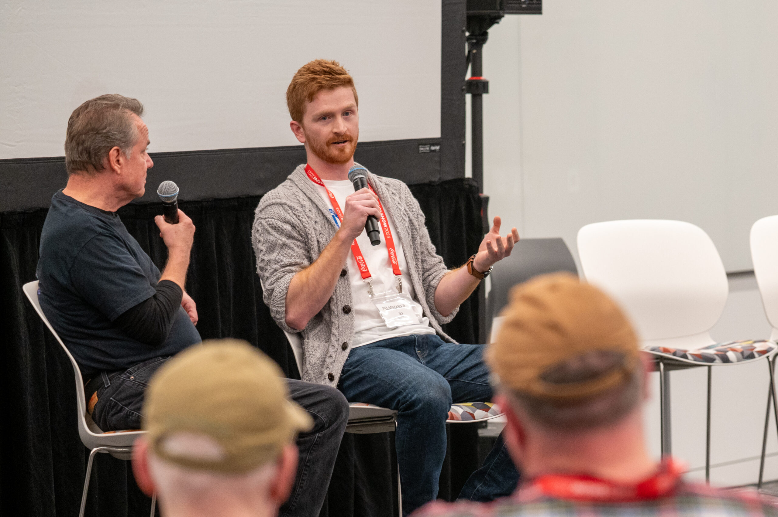 Two men on a panel speaking into handheld microphones during a discussion, audience visible in the foreground.